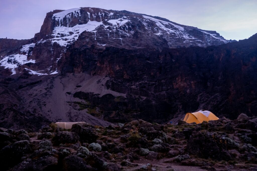 Tent among rocks below the snowy summit of Kilimanjaro
