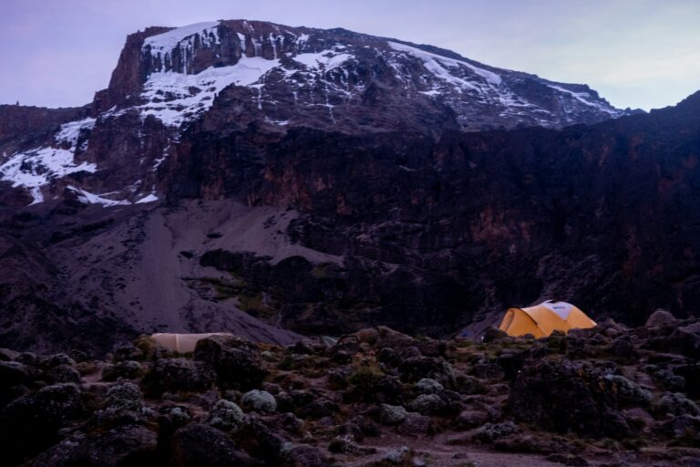 Tent among rocks below the snowy summit of Kilimanjaro